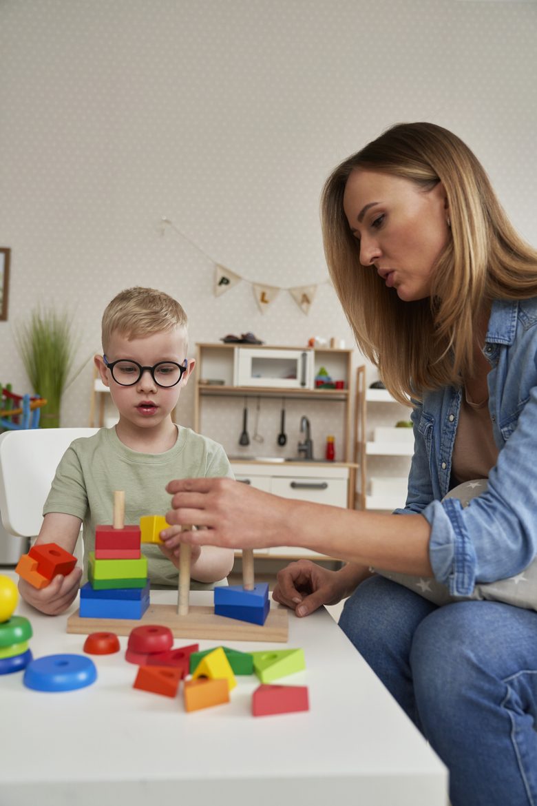 A therapist guiding a young boy stacking wooden blocks