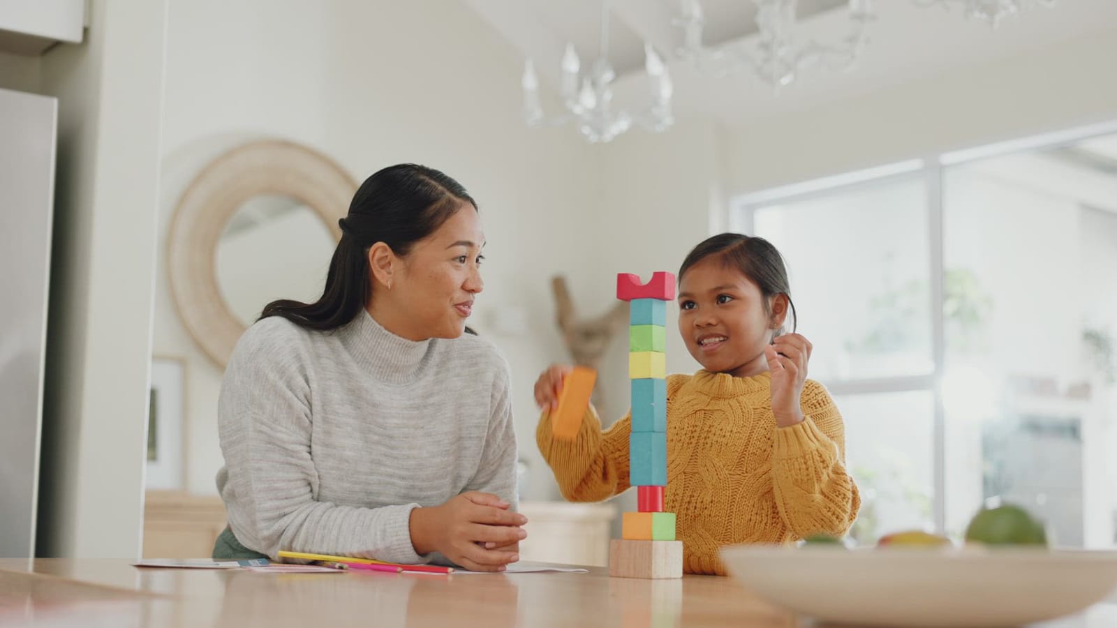 A caregiver and child building a tower of colorful blocks together